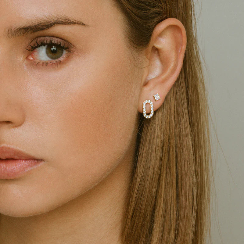 Close-up of a woman wearing a diamond hoop earring on a neutral background