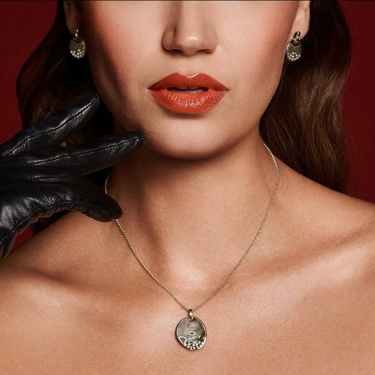 Close-up of a woman's neck with a necklace and earrings, wearing a black glove.