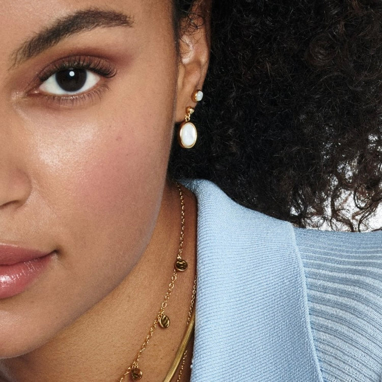 Close-up of a woman wearing gold earrings and a necklace with a light blue garment.
