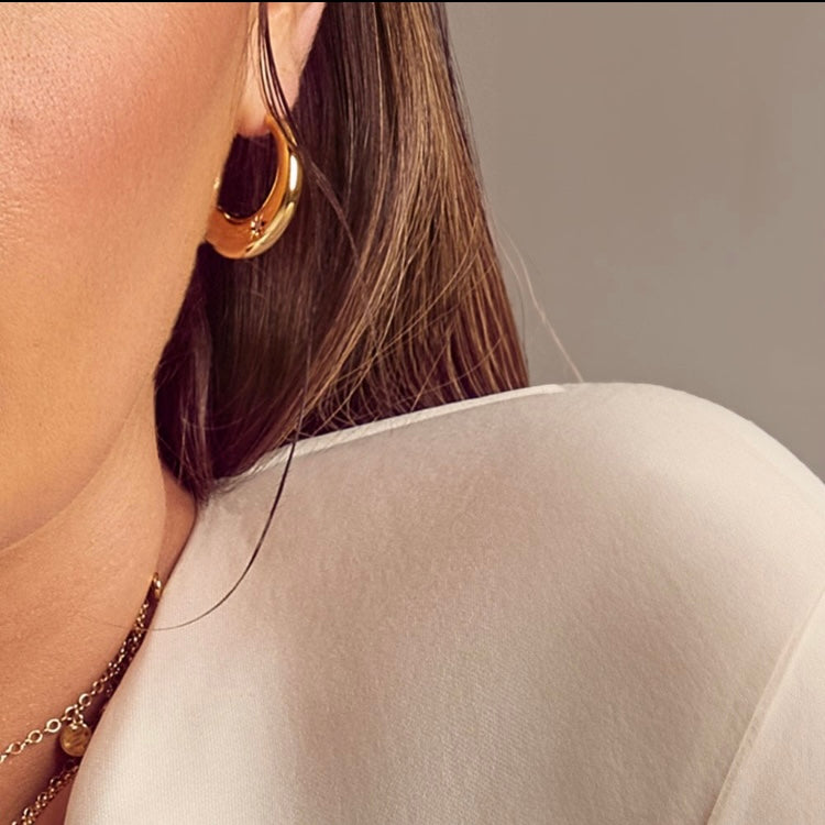 Close-up of a person wearing gold hoop earrings and a beige top.